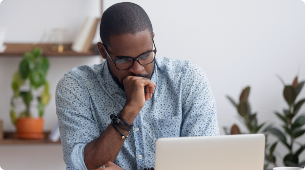 Man in glasses thoughtfully looking at laptop screen at home.
