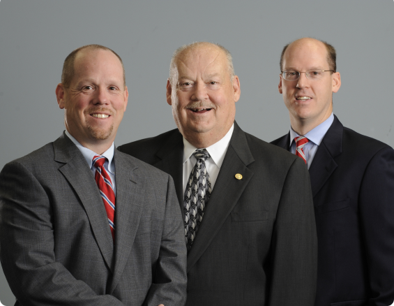 Three men in suits stand together, smiling. Professional business portrait.