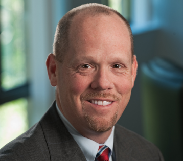 John A. Hackett, Jr., CIC, headshot wearing a suit and tie, smiling.