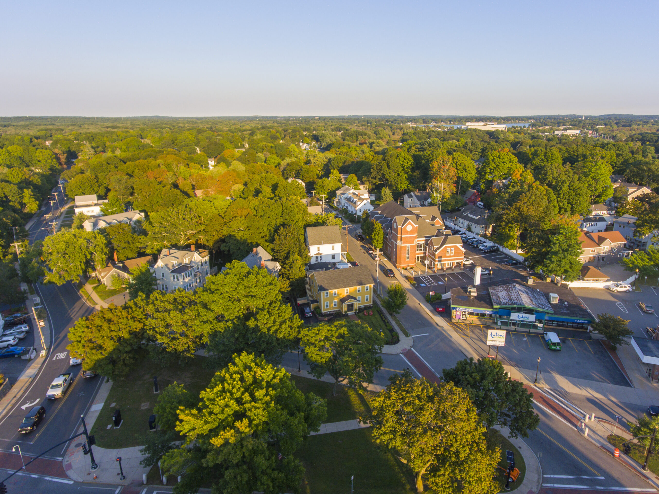 Aerial view of a charming town square with brick buildings, green trees, and a blue sky.
