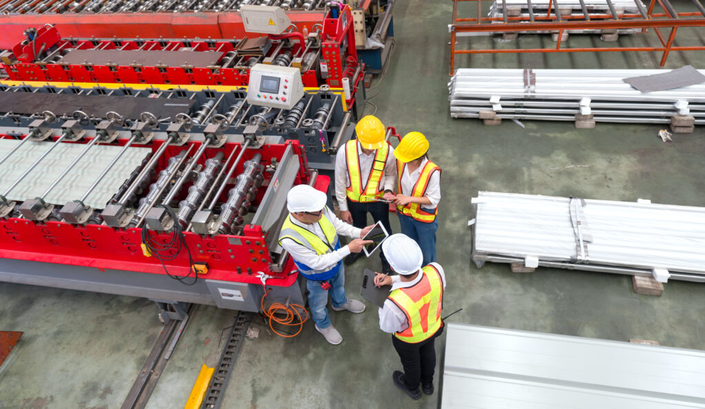 Factory workers review commercial lines on a tablet near industrial machinery.